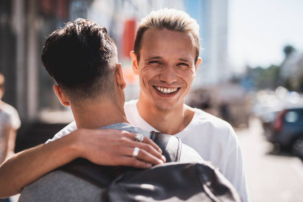 Satisfied friends embracing during meeting at street - Фото, изображение