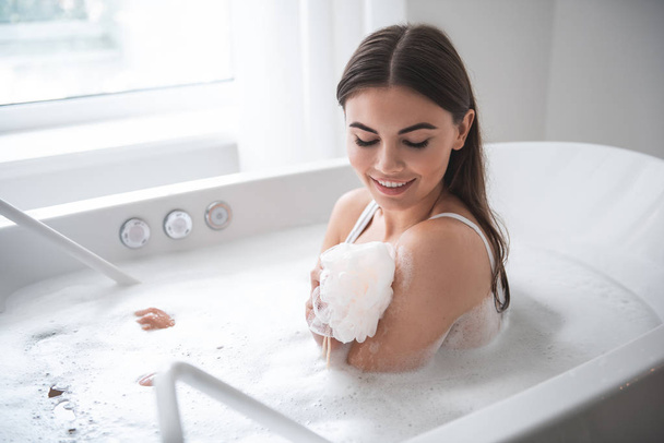 Pleased female washing body with shower sponge - Φωτογραφία, εικόνα