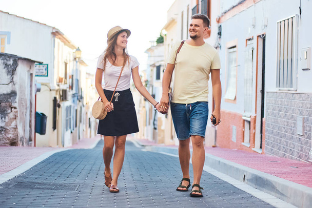Young happy couple walking holding each others hand in Spanish town Denia. Stylish man and woman on vacations in Spain, Europe. Tourism and travelling concept. - Фото, зображення
