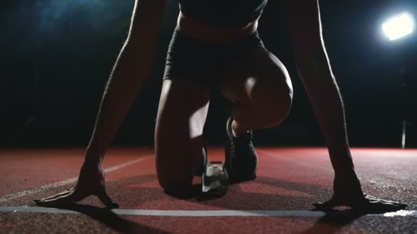 Zawodnik profesjonalny kobiety na ciemnym tle gotovtes uruchomić sprint buty biegowe w trampki na torze stadionu na ciemnym tle. Z bliska - Materiał filmowy, wideo