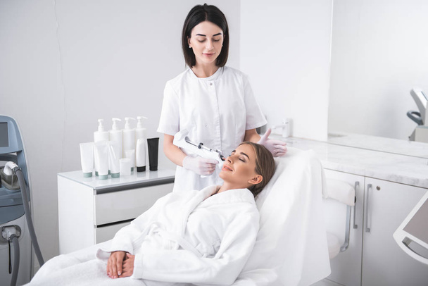 Smiling young woman at cosmetologist cabinet getting injection - Fotografie, Obrázek