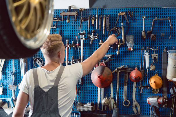 Вид сзади на человека, выбирающего полезный инструмент во время работы в ремонтной мастерской
 - Фото, изображение