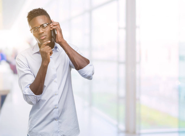 Hombre afroamericano joven usando teléfono inteligente cara seria pensando en la pregunta, idea muy confusa
 - Foto, Imagen