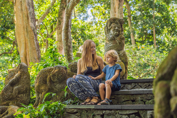 Mom and son travelers sitting on stairs with sculptures in Ubud forest, Bali Indonesia - Foto, immagini