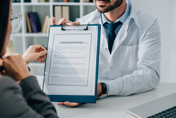 oříznutý obraz všeobecného lékaře ukazující formuláři pojistného nároku pacienta v klinice - Fotografie, Obrázek