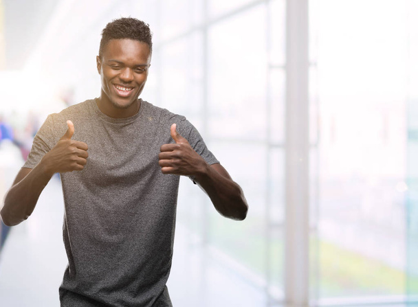 Young african american man wearing grey t-shirt success sign doing positive gesture with hand, thumbs up smiling and happy. Looking at the camera with cheerful expression, winner gesture. - Photo, image