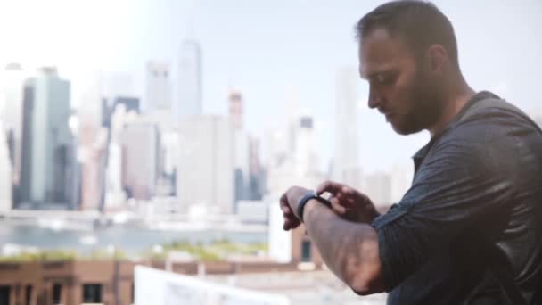 Un exitoso hombre de negocios europeo sonriendo, usando un reloj inteligente para comunicarse en el épico horizonte de Manhattan, Nueva York
. - Metraje, vídeo