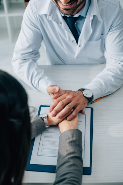 image recadrée du patient et du médecin tenant la main au-dessus du formulaire de demande d'assurance en clinique
 - Photo, image