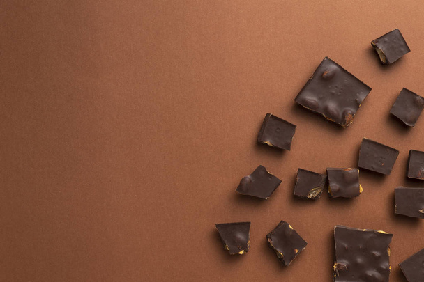 Dark chocolate pieces with roasted almonds scattered around on brown background - Foto, Bild