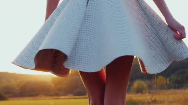 Μια νεαρή λεπτή γυναίκα με ένα ελαφρύ φούστα γυρίζοντας σε ένα λιβάδι. Κατά το ηλιοβασίλεμα, αργή κίνηση βίντεο 4k - Πλάνα, βίντεο