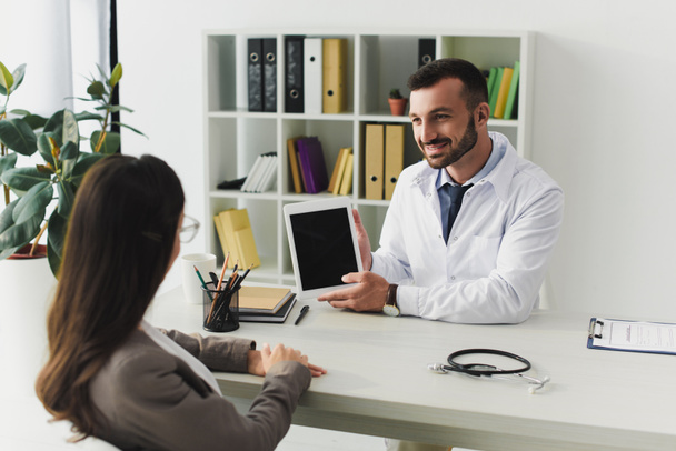 sonriente doctor mostrando paciente gadget con pantalla en blanco en clínica
 - Foto, imagen