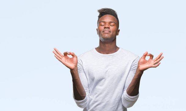 Jonge Afro-Amerikaanse man over geïsoleerde achtergrond ontspannen en lachend met ogen gesloten doen meditatie gebaar met vingers. Yoga concept. - Foto, afbeelding
