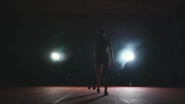 暗い背景に暗い背景にスタジアムのトラックでスニーカーでジョギング シューズのスプリントを実行するプロの女性アスリート - 映像、動画
