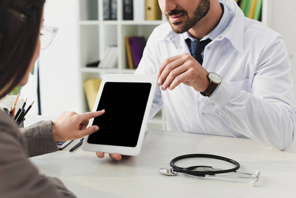 cropped image of doctor showing patient tablet with blank screen in clinic - 写真・画像