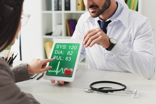 bijgesneden afbeelding van arts tonen patiënt tablet met pulse toestel in kliniek - Foto, afbeelding