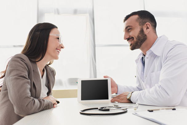 médico sorridente mostrando tablet paciente com tela em branco na clínica
  - Foto, Imagem