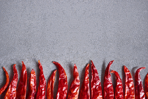 bovenaanzicht van gedroogde rode chilipepers gerangschikt op grijs tafelblad - Foto, afbeelding