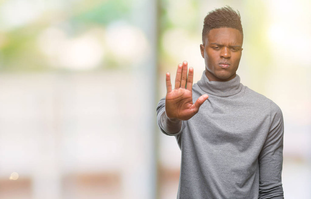 Jonge Afro-Amerikaanse man over geïsoleerde achtergrond stop doen zingen met de palm van de hand. Waarschuwing expressie met negatieve en ernstige gebaar op het gezicht. - Foto, afbeelding
