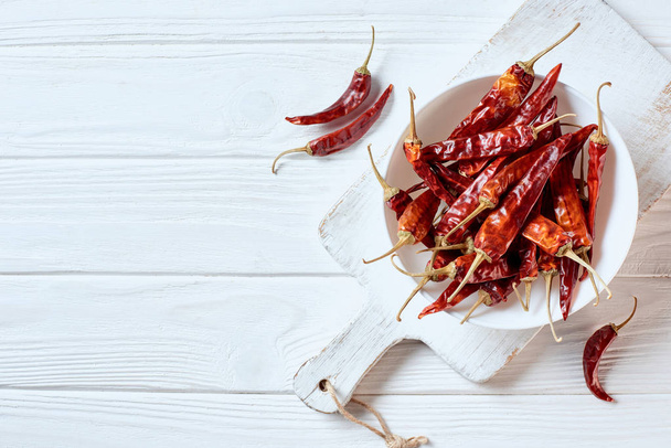 top view of dried cayenne peppers in bowl on white cutting board on wooden surface - 写真・画像