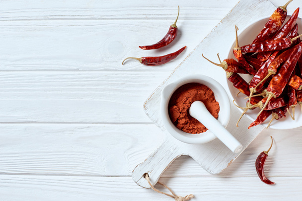 flat lay with grinded chili pepper in mortar with pestle on cutting board on white wooden surface - Photo, Image