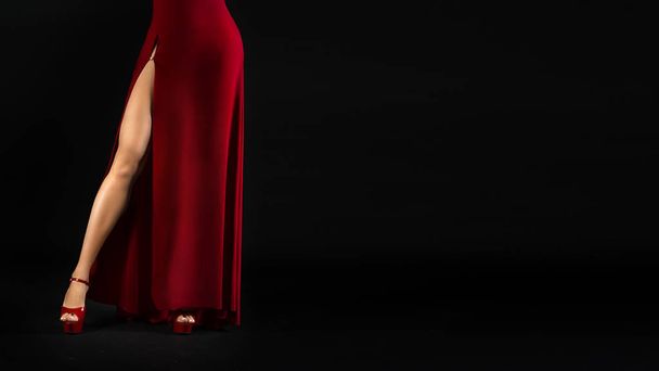 gambe femminili sexy irriconoscibili in un abito rosso e scarpe con tacco alto su uno sfondo nero
. - Foto, immagini