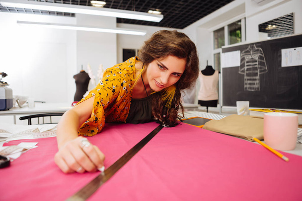 Experienced dressmaker leaning on the table and looking at the fabric - Foto, Imagen