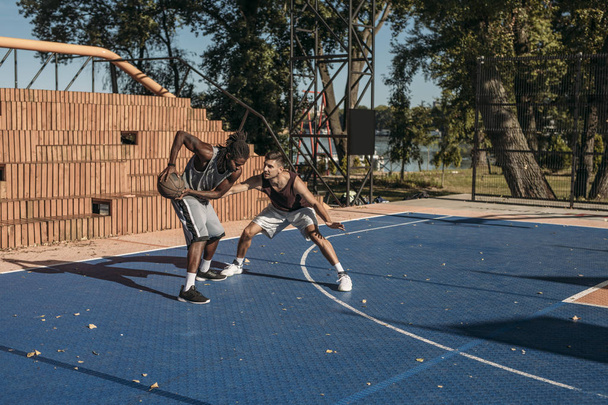 Two handsome men playing basketball outdoors. - Fotografie, Obrázek
