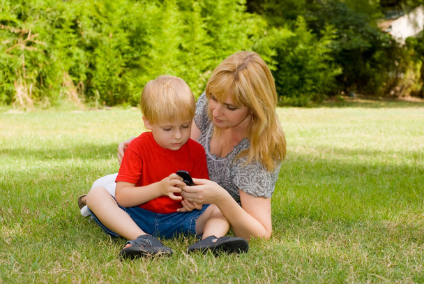 мати і син лежать на траві і використовують мобільний телефон в парку
 - Фото, зображення