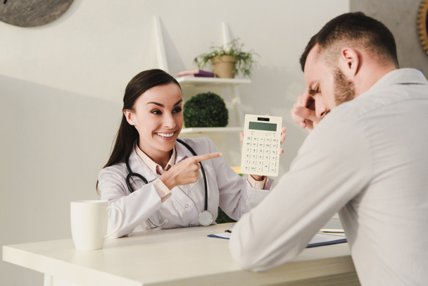 усміхнений клієнт і професійний лікар підрахунок фінансів на калькуляторі страхування життя в офісі
 - Фото, зображення