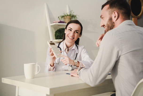 улыбающийся клиент и врач подсчитывают финансы на калькуляторе для медицинского страхования
   - Фото, изображение