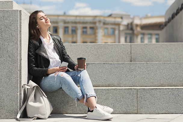 Boldog hétköznapi lány, hallgató-hoz zene-a smartphone és a kávéfogyasztás szabadban - Fotó, kép