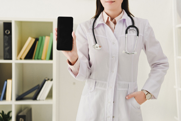 vista recortada de la doctora presentando smartphone con pantalla en blanco
 - Foto, imagen