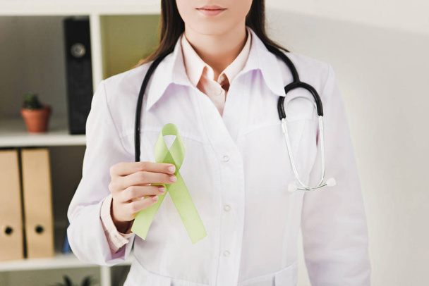 cropped view of doctor in white coat with stethoscope holding green ribbon - mental health day - Foto, Imagen
