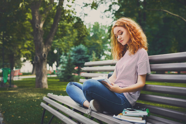 Ruda młoda kobieta z notebookiem na ławce w parku - Zdjęcie, obraz