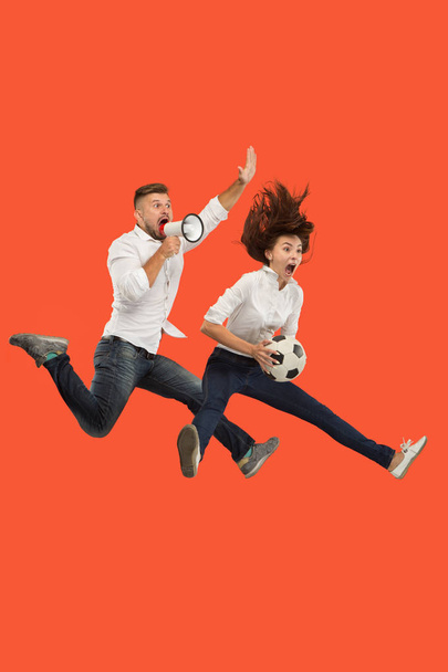 Forward to the victory.The young couple as soccer football player jumping and kicking the ball at studio on a red - Foto, Bild