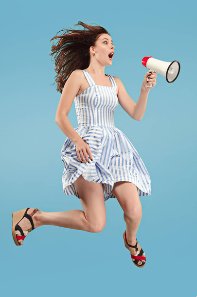 Beautiful young woman jumping with megaphone isolated over blue background - Photo, Image