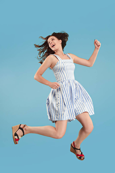 Freedom in moving. Pretty young woman jumping against blue background - 写真・画像