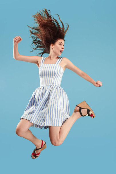 Freedom in moving. Pretty young woman jumping against blue background - Foto, Bild