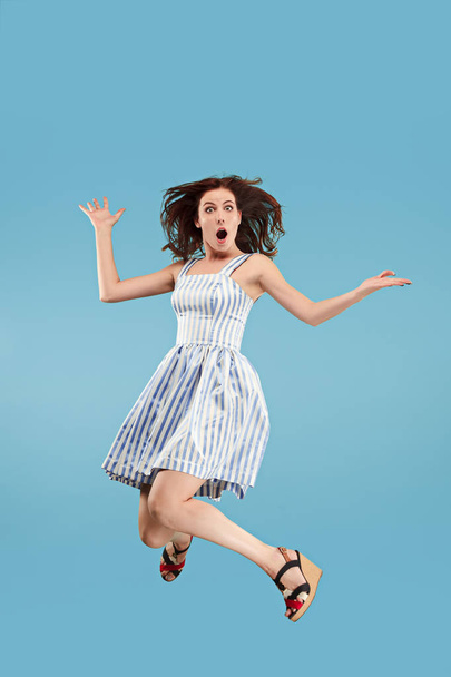 Freedom in moving. Pretty young woman jumping against blue background - Фото, зображення