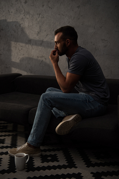 thoughtful man sitting on sofa with coffee cup on floor - Foto, Imagem