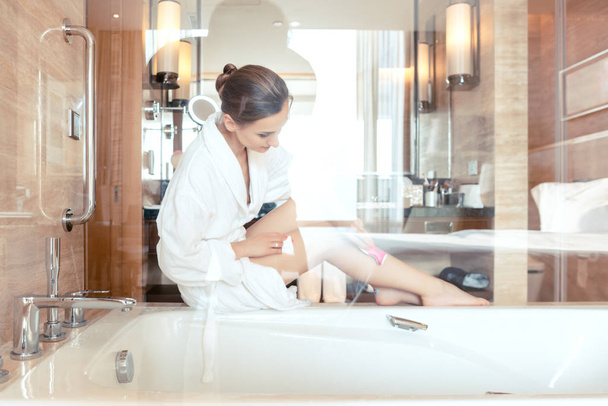 Mulher removendo o cabelo raspando as pernas no banheiro do hotel
 - Foto, Imagem