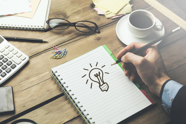 man drawing lighting bulb on notebook with stationary on table - Photo, Image