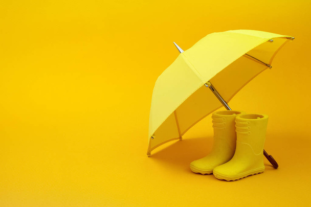 A pair of yellow rain boots and a umbrella on a yellow - Zdjęcie, obraz