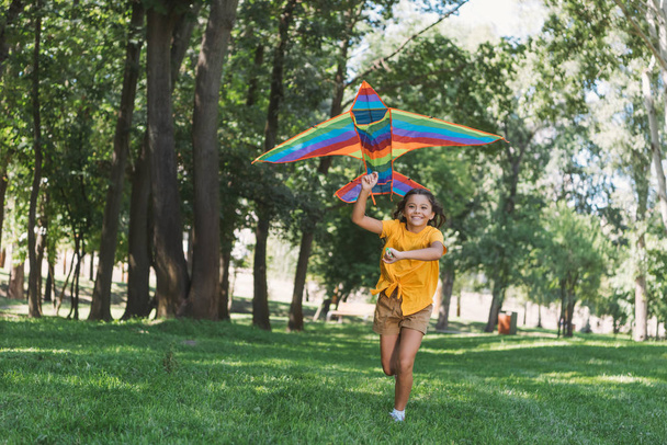 hermoso feliz niño sosteniendo colorido cometa y corriendo en parque
 - Foto, Imagen