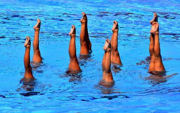 Gesynchroniseerde zwemmers punt omhoog uit het water in actie. Gesynchroniseerde zwemmers benen beweging. Gesynchroniseerde zwemmende team het uitvoeren van een gesynchroniseerde routine van ingewikkelde bewegingen in het water. - Foto, afbeelding