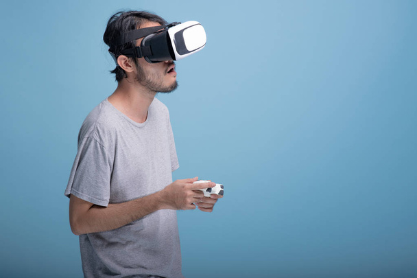 Young bearded man playing VR game in blue background. Bored Asian young hipster wearing VR headset, half body shot. Young generation hipster relaxation concept. - Fotoğraf, Görsel