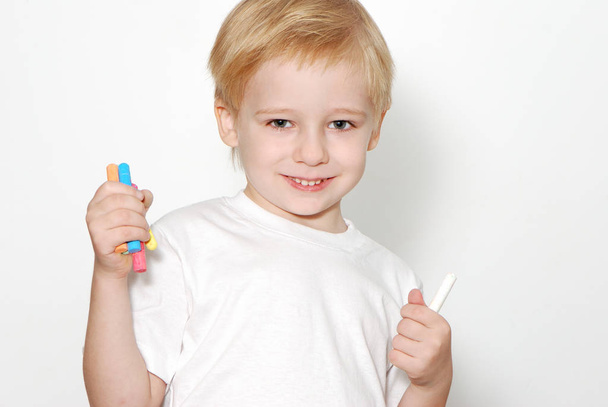 Portrait of cute blonde boy holding color pencils standing isolated on white background - Фото, изображение