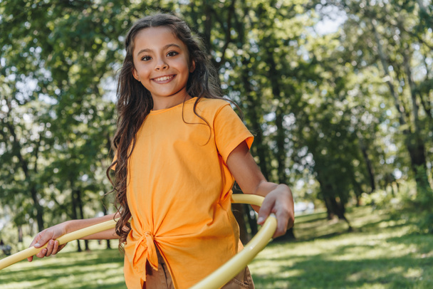entzückendes glückliches Kind, das mit Hula-Hoop-Reifen spielt und im Park in die Kamera lächelt - Foto, Bild