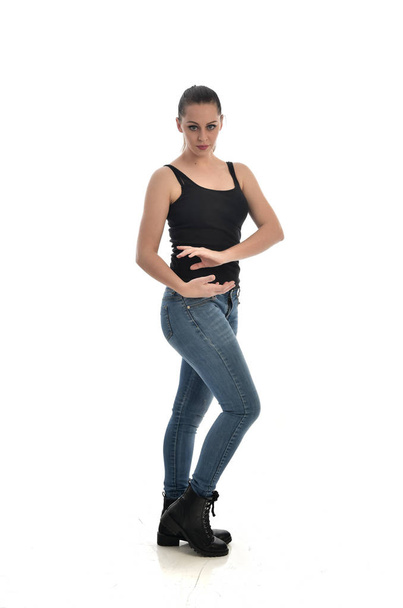 full length portrait of brunette girl wearing black single and jeans. standing pose, side profile. isolated on white studio background. - Photo, Image