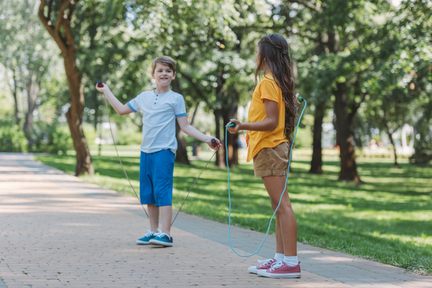 χαριτωμένο χαρούμενα παιδιά που παίζουν με παρακάμπτοντας τα σχοινιά στο πάρκο - Φωτογραφία, εικόνα